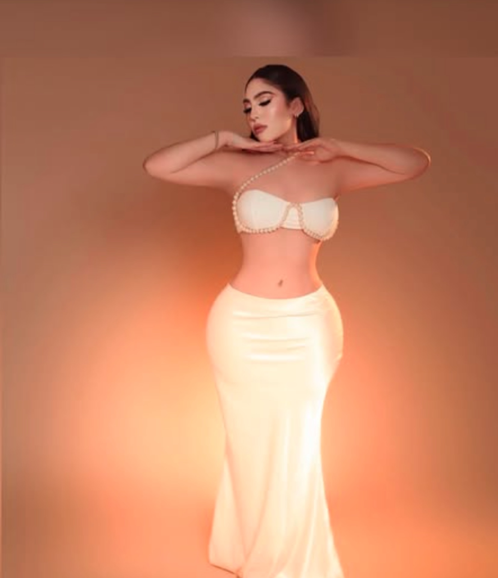 Paciente real de A+ Plastic Surgery con vestido blanco satinado, estudio